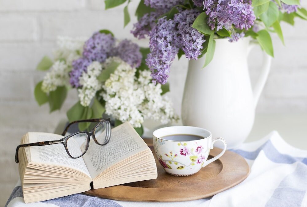 Table with lilacs in vase, book, glasses, and cup of tea