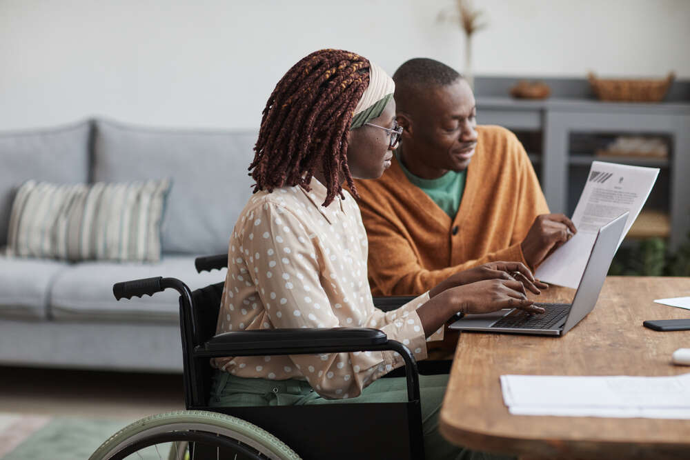 teenager with special needs working at a computer with an older caregiver beside her