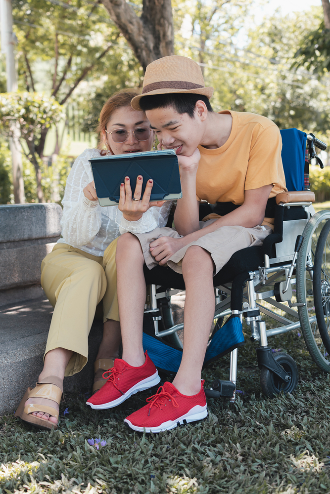 special needs teenager sitting in wheelchair reading with a caregiver