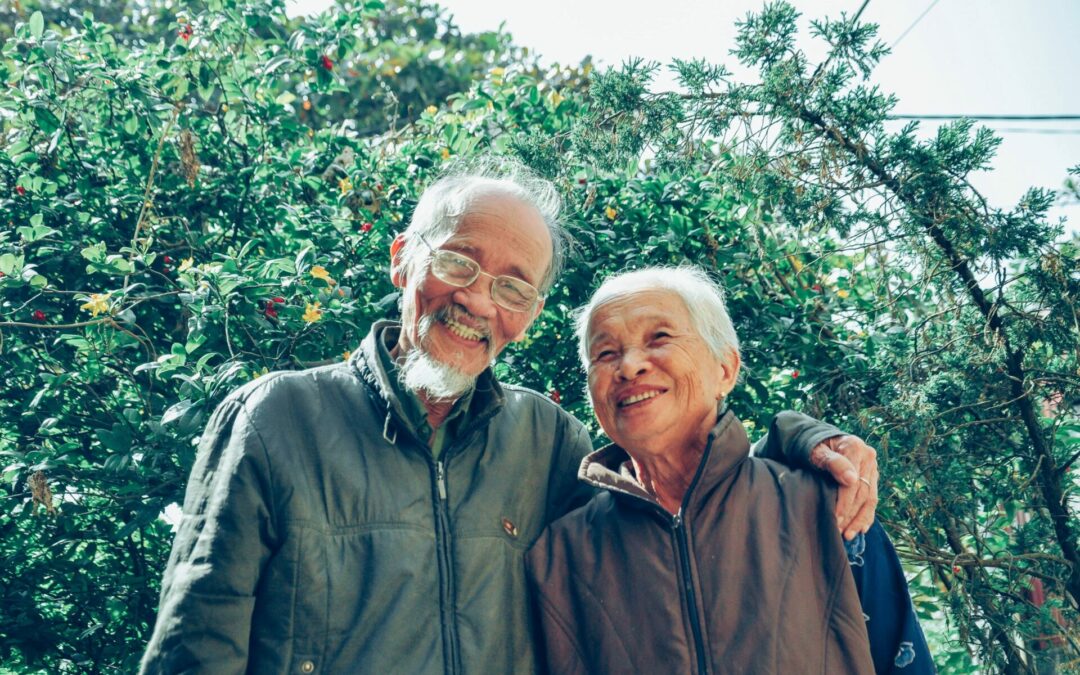 Elderly couple standing in front of a tree with arms embraced