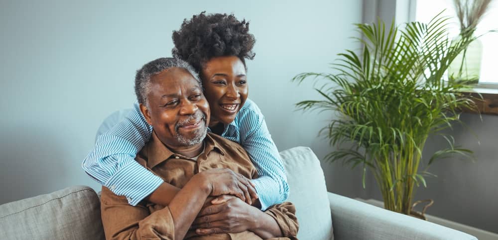 Daughter and elderly father embracing while sitting on the couch